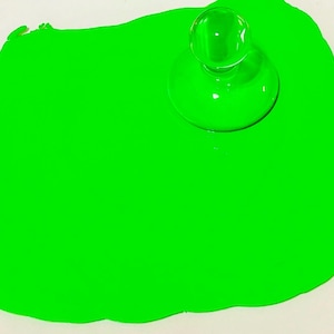 Può includere: Un design astratto verde brillante con un oggetto di vetro trasparente e arrotondato sopra. Il colore verde domina l'immagine, creando un contrasto visivo sorprendente con lo sfondo bianco.
