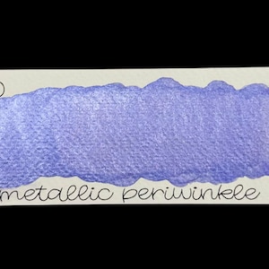 May include: A swatch of metallic periwinkle watercolor paint on a white rectangular card. The card has the text "no. 150" and "metallic periwinkle" in black script. The paint is a shimmering, light purple color.