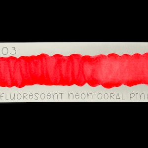 May include: A rectangular swatch of paper with a vibrant neon coral pink paint stroke. The text "no. 203" is at the top left, and "FLUORESCENT NEON CORAL PINK" is written below the paint stroke. The background is black.