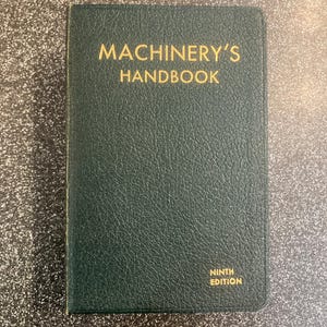 May include: A dark green book with the title "MACHINERY'S HANDBOOK" in gold lettering. The cover has a textured finish. The words "NINTH EDITION" are printed in gold at the bottom right corner.