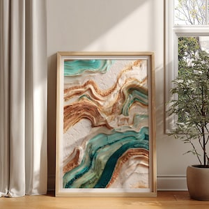 May include: Abstract art print in a wooden frame. The artwork features flowing patterns in shades of teal, brown, and gold against a white background. The framed art is displayed on a wooden floor, next to a window and a potted plant.
