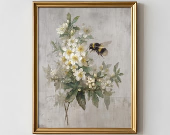Può includere: Una stampa artistica incorniciata raffigurante un grappolo di fiori bianchi con centri gialli e foglie verdi su uno sfondo grigio chiaro strutturato. Un bombo con strisce nere e gialle è raffigurato in volo vicino ai fiori. L'opera è racchiusa in una cornice in metallo dorato. Il testo Novera Prints è visibile in basso.