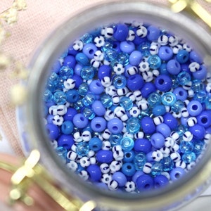 Könnte beinhalten: Ein Glasgefäß gefüllt mit blauen und weißen Perlen. Die Perlen sind eine Mischung aus Volltonfarben und gemusterten Designs.