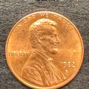 Puede incluir: Una moneda de cobre de 1932, un centavo Lincoln, con el perfil de Abraham Lincoln mirando hacia la derecha. Se ven las palabras "IN GOD WE TRUST" y "LIBERTY". También se muestra el año "1932". El número "00114" está en la esquina superior izquierda.