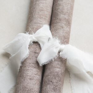 Op de afbeelding: Twee bruine stofrollen die met een wit, gescheurd lint aan elkaar zijn gebonden. Het lint is in een strik geknoopt.