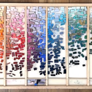 May include: A wooden tray filled with rectangular pastel chalks, arranged in vertical columns by color. The colors range from dark browns and grays to vibrant yellows, pinks, blues, greens, and yellows. The chalks are of varying sizes and shapes.