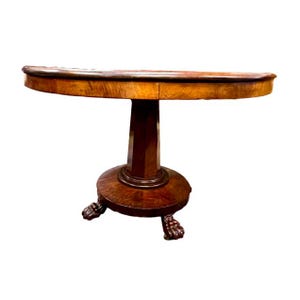 May include: A semi-circular wooden console table featuring a polished light brown top with a visible wood grain. The table is supported by a central pedestal column that rests on a circular base with three carved feet shaped like animal paws.