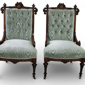 May include: Two antique high-back chairs with ornate dark wood frames. The chairs feature light green patterned upholstery and button tufting on the backs. The legs are dark wood with decorative carvings, and the chairs have a classic, elegant design.