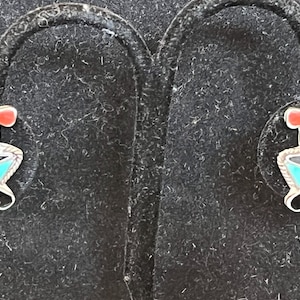 May include: A pair of silver earrings with a colorful bird design. The birds are made of turquoise, red, white, and black stones.