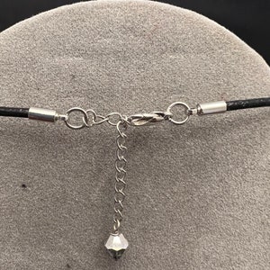 Op de afbeelding: Een zilveren ketting met een klein kristallen hanger en een zwart leren koord met een zilveren sluiting.