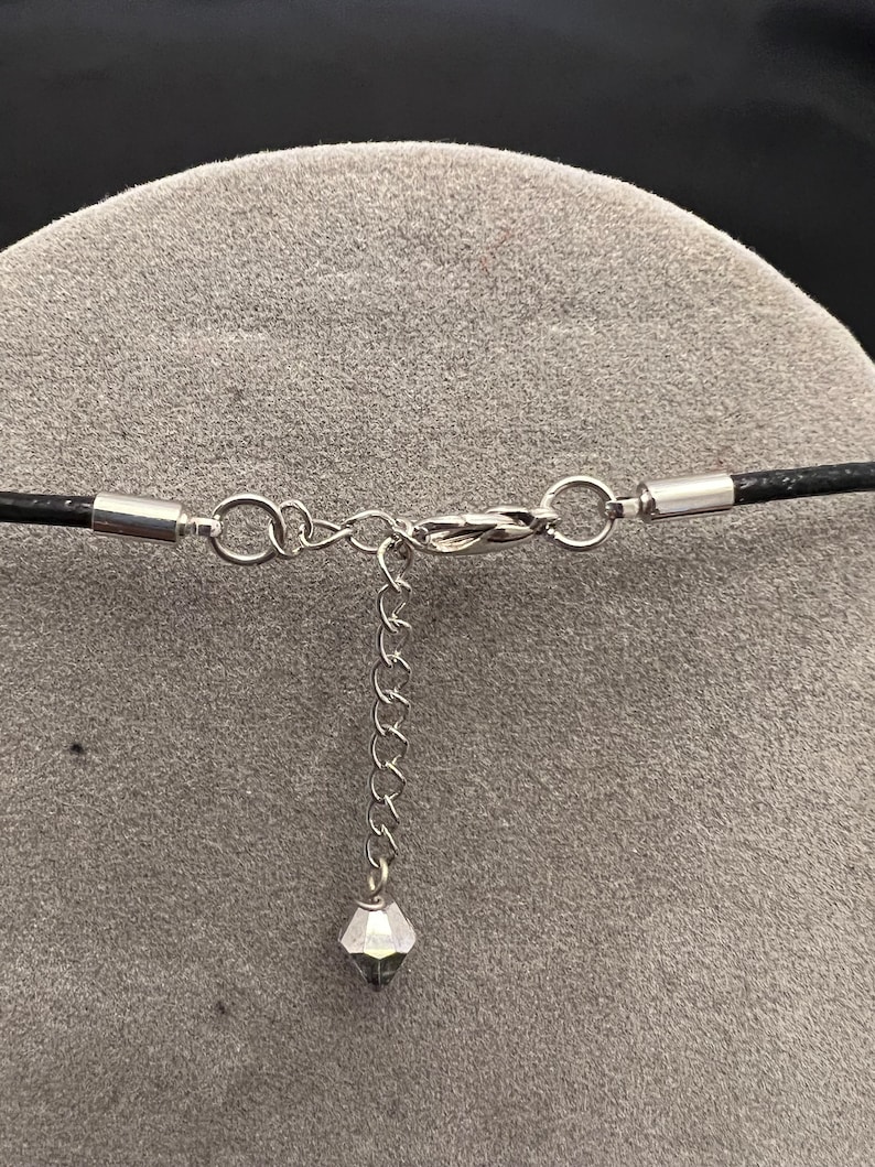 Op de afbeelding: Een zilveren ketting met een klein kristallen hanger en een zwart leren koord met een zilveren sluiting.