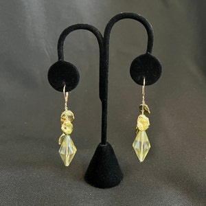 May include: A pair of gold dangle earrings with a clear crystal teardrop shape at the bottom. The earrings feature multiple gold and green iridescent shell-like discs.