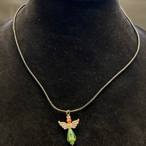 Op de afbeelding: Een zilveren engel hanger ketting met een groene en rode kristallen hanger. De ketting is aan een zwart lederen koord.