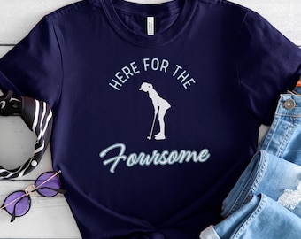 May include: Navy blue t-shirt with a white silhouette of a woman golfing and the text "Here for the Foursome".