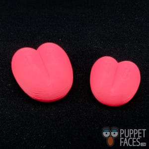 May include: Two bright pink, heart-shaped objects are displayed against a black background. The objects have a smooth texture and a rounded shape, with a distinct indentation at the top, resembling a split heart. The objects vary in size.