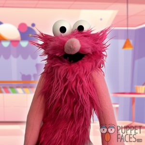 May include: A pink furry puppet with large white eyes and a pink nose. The puppet is smiling and has a long pink beard.
