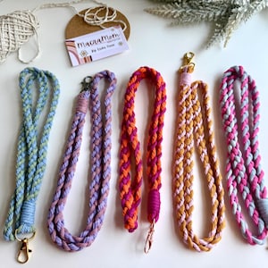 May include: Five braided macrame lanyards in various colors: blue, purple, orange, yellow, and pink. Each lanyard has a gold-colored clasp. A tag with the text "MacraMom" is also visible.