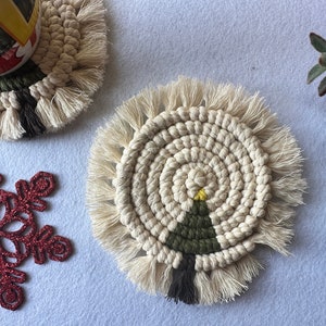 May include: Two handmade crocheted coasters with fringe. One coaster features a green and yellow Christmas tree design.