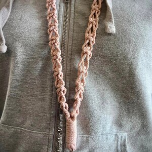 Model wearing style 3, the weaved pattern, in a muted pink color. The keychain clasp reaches around bellybutton area.