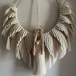 May include: A macrame angel wall hanging with a gold hoop and a long tassel. The angel is made with natural colored cotton cord and has a delicate, bohemian style.