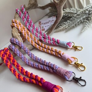 Peut inclure: Quatre lani&egrave;res macram&eacute; aux tons de rose, orange, violet et beige. Chaque lani&egrave;re est tress&eacute;e avec une combinaison de couleurs diff&eacute;rente et comporte un fermoir en m&eacute;tal. Les lani&egrave;res sont pr&eacute;sent&eacute;es sur une surface blanche.