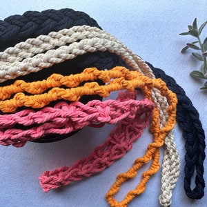 Peut inclure: Plusieurs sangles en coton tress&eacute; color&eacute;es, dans des tons de marine, cr&egrave;me, orange et rose. Les sangles sont dispos&eacute;es en cercle, mettant en valeur leur texture et leur design. Quelques sangles pendent, montrant leur longueur.