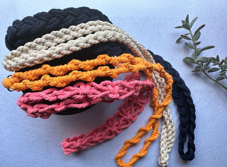 Peut inclure: Plusieurs sangles en coton tress&eacute; color&eacute;es, dans des tons de marine, cr&egrave;me, orange et rose. Les sangles sont dispos&eacute;es en cercle, mettant en valeur leur texture et leur design. Quelques sangles pendent, montrant leur longueur.