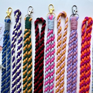 Peut inclure: Une collection de lani&egrave;res macram&eacute; faites &agrave; la main, aux couleurs vari&eacute;es : bleu, violet, vert, noir, rose, orange et jaune. Chaque lani&egrave;re pr&eacute;sente un motif tress&eacute; et un fermoir en m&eacute;tal pour attacher des cl&eacute;s ou un badge. Pr&eacute;sent&eacute;es sur fond blanc.