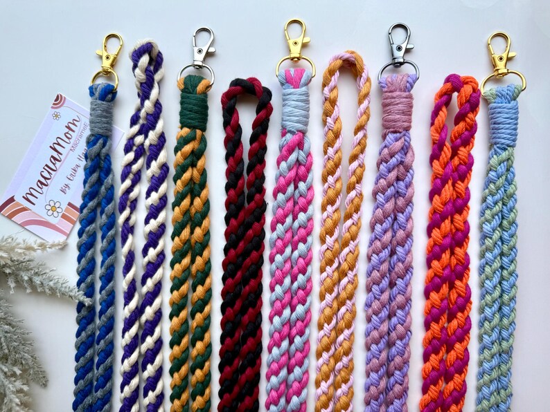 Peut inclure: Une collection de lani&egrave;res macram&eacute; faites &agrave; la main, aux couleurs vari&eacute;es : bleu, violet, vert, noir, rose, orange et jaune. Chaque lani&egrave;re pr&eacute;sente un motif tress&eacute; et un fermoir en m&eacute;tal pour attacher des cl&eacute;s ou un badge. Pr&eacute;sent&eacute;es sur fond blanc.