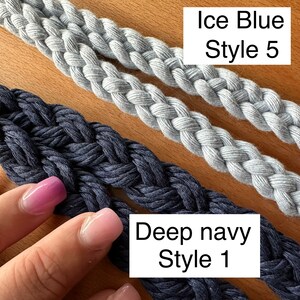 Two blue macrame lanyards, showing style 1 and style 5. 1 is deep navy braid, style 5 is a celtic 4 strand round braid in color ice blue. They are laid out flat on a wooden background.l
