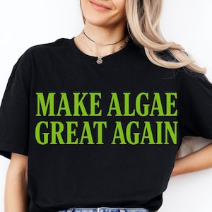 Könnte beinhalten: Ein schwarzes T-Shirt mit kurzen Ärmeln und dem Text "MAKE ALGAE GREAT AGAIN", der in einer kräftigen, hellen lindgrünen serifenlosen Schrift auf der Brust gedruckt ist. Das Kleidungsstück hat einen klassischen Rundhalsausschnitt und eine Standardpassform.