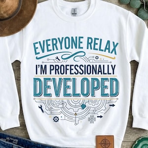 Peut inclure: Un sweat-shirt blanc à manches longues et col rond portant l'inscription "EVERYONE RELAX I'M PROFESSIONALLY DEVELOPED" en bleu et bleu foncé. Le motif comprend des éléments graphiques de rouages, de circuits et de petits outils.