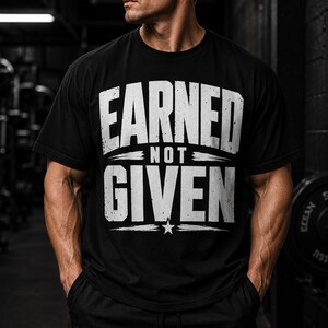 Könnte beinhalten: Schwarzes T-Shirt mit dem Text "EARNED NOT GIVEN" in abgenutzten weißen Buchstaben. Das Design beinhaltet eine Stern-Grafik. Das Shirt ist kurzärmlig und vermutlich aus Baumwolle.