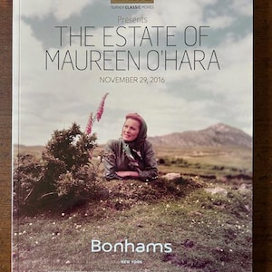 May include: A book cover featuring the text "THE ESTATE OF MAUREEN O'HARA" with "TCM" and "Bonhams" logos. The cover image shows a woman in a headscarf in a field. The date "NOVEMBER 29, 2016" is also displayed.