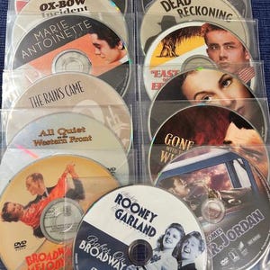 May include: A collection of DVDs featuring classic films like "The Ox-Bow Incident," "Marie Antoinette," and "Babes on Broadway." The discs are in clear plastic sleeves, showcasing movie titles and actors' faces. The DVDs are arranged on a blue surface.