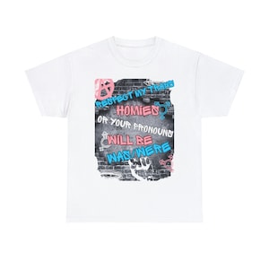 Peut inclure: T-shirt blanc avec un imprimé graphique d'un mur de briques avec des graffitis qui disent "Respect my trans homies or your pronouns will be was/were".