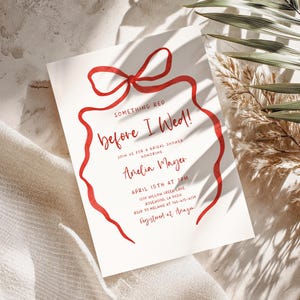 Puede incluir: Una tarjeta de invitación blanca con texto rojo y un diseño de lazo rojo. El texto dice "Something Red before I Wed!" e incluye detalles para una despedida de soltera, incluyendo la fecha, hora y lugar.