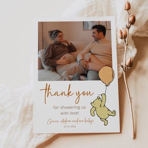 Pode incluir: Um cart&atilde;o de agradecimento com uma foto de uma mulher gr&aacute;vida e um homem. O cart&atilde;o apresenta um desenho animado do Winnie the Pooh segurando um bal&atilde;o. O texto do cart&atilde;o diz "Obrigado por nos dar uma chuva de amor! Grace, Adam e nosso beb&ecirc;! 22-01-2024"