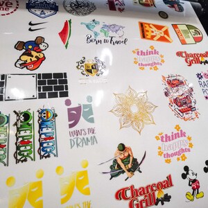 May include: A sheet of white vinyl with various colourful stickers featuring different designs and text. Some of the stickers include a cartoon character, a watermelon, a flower, a cartoon character, a brick wall, a logo, and a cartoon character with a sword. The text on the stickers includes "Born to Travel", "Think Happy Thoughts", "Charcoal Grill", "Radiate Positivity", "What's the Drama", and "Think Happy Thoughts".