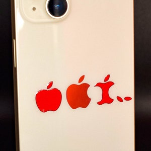 May include: A white smartphone with a red apple logo sticker on the back. The sticker shows a progression of the apple logo, starting with a whole apple and ending with a bitten apple.