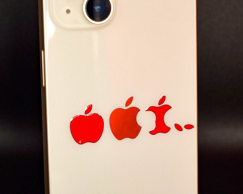 May include: A white smartphone with a red apple logo sticker on the back. The sticker shows a progression of the apple logo, starting with a whole apple and ending with a bitten apple.