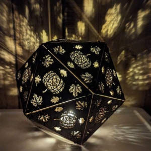 May include: A black geometric lamp with a light inside, casting shadows of leaves and pumpkins on the wall. The lamp is made of wood and has a delicate, intricate design.