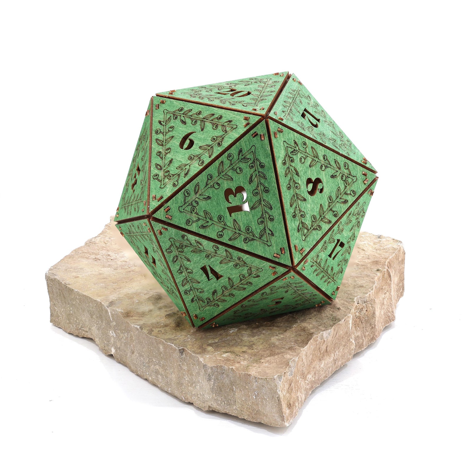 A green wooden icosahedron 20-sided sculpture with vines and numbers engraved on each side sits on a faux-rock pedestal.