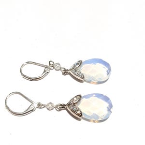 May include: A pair of silver-toned drop earrings. Each earring features a faceted, pear-shaped, opalescent gemstone. The gemstones are accented with a leaf-shaped design encrusted with small, clear crystals. The earrings have lever-back closures.