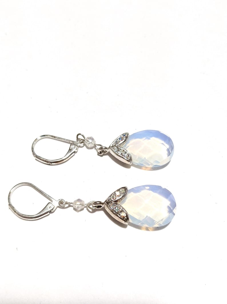 May include: A pair of silver-toned drop earrings. Each earring features a faceted, pear-shaped, opalescent gemstone. The gemstones are accented with a leaf-shaped design encrusted with small, clear crystals. The earrings have lever-back closures.