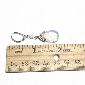 May include: A single silver earring with a pear-shaped, opalescent gemstone. The earring is approximately 1 inch (2.5 cm) long, with a small cluster of clear stones and a decorative silver accent at the top.
