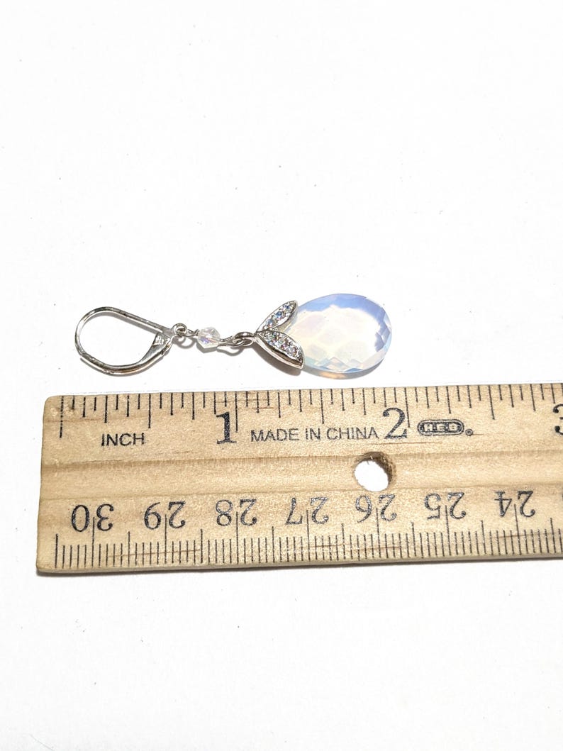 May include: A single silver earring with a pear-shaped, opalescent gemstone. The earring is approximately 1 inch (2.5 cm) long, with a small cluster of clear stones and a decorative silver accent at the top.