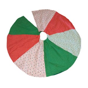 May include: Circular Christmas tree skirt with alternating red, green, and patterned panels. The patterned panels feature candy cane and floral designs. The skirt has a central opening for the tree trunk.