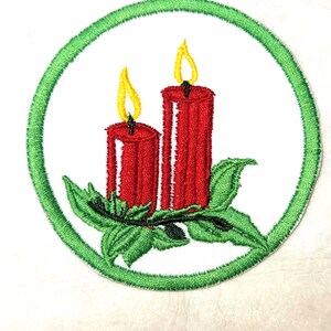 May include: Embroidered patch featuring two red candles with yellow flames, set against a white background. The candles are surrounded by green leaves and a green circular border. A festive, holiday-themed design.