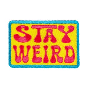 May include: A rectangular embroidered patch featuring the text STAY WEIRD in bold pink letters against a bright yellow background, all enclosed within a thick, vibrant turquoise blue border that frames the entire design clearly.